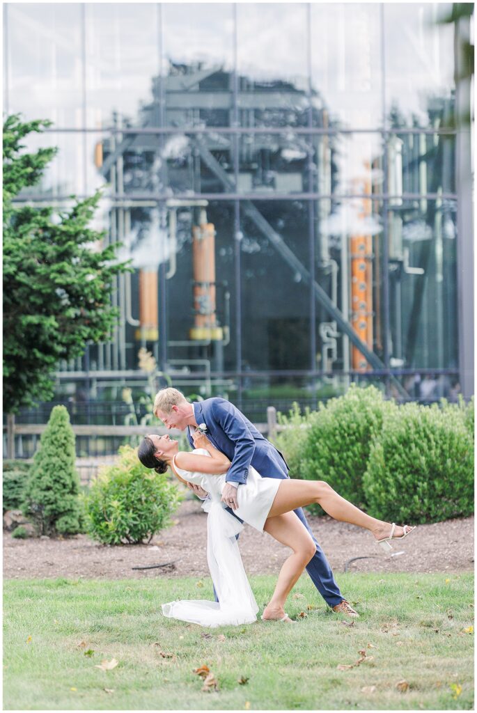 Groom dips the bride back in a playful kiss in front of a glass building, photographed by a Boston Elopement Photographer.