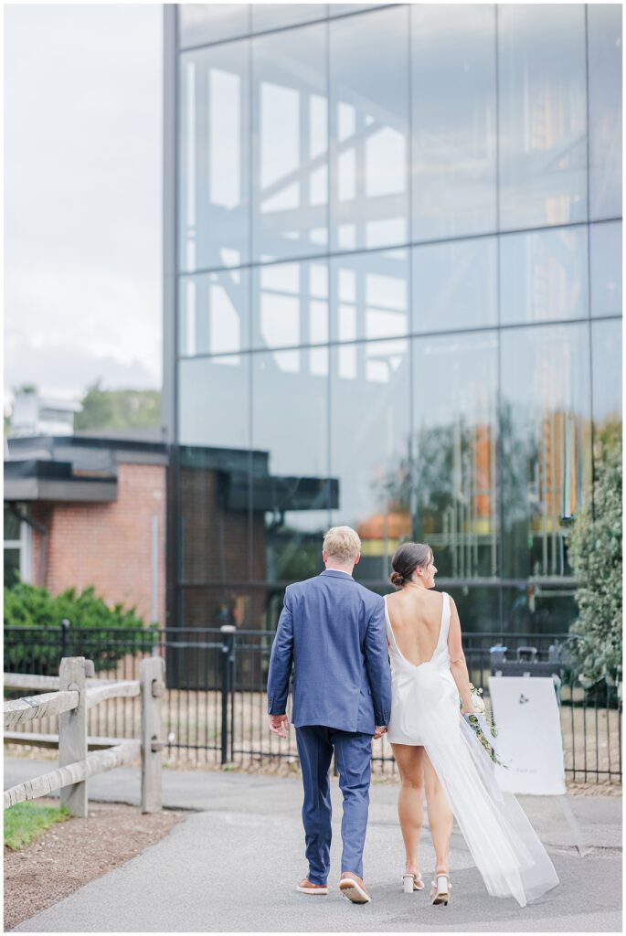 Couple walking away hand in hand toward a glass-walled building during their Boston elopement.