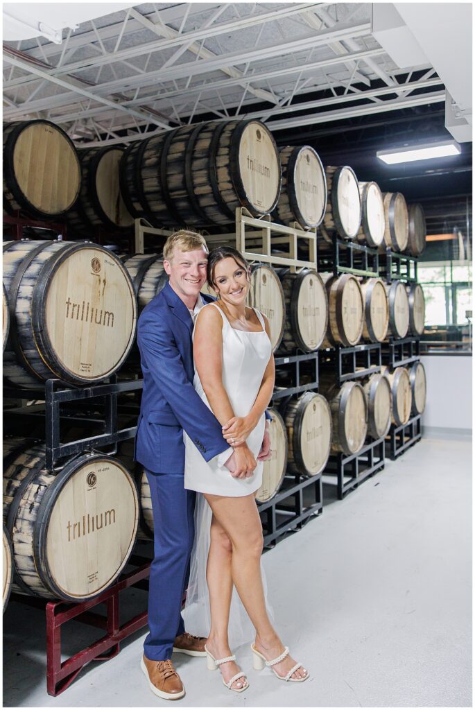 Couple standing in front of stacked wooden barrels, embracing and smiling for their Boston elopement photos.