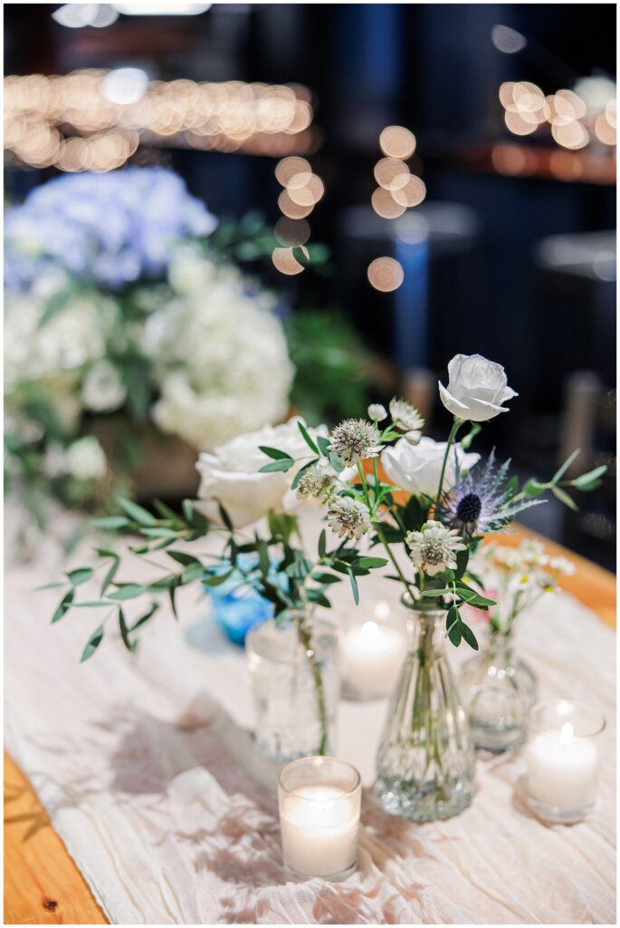 Detail of floral centerpieces and candles on a wooden reception table.