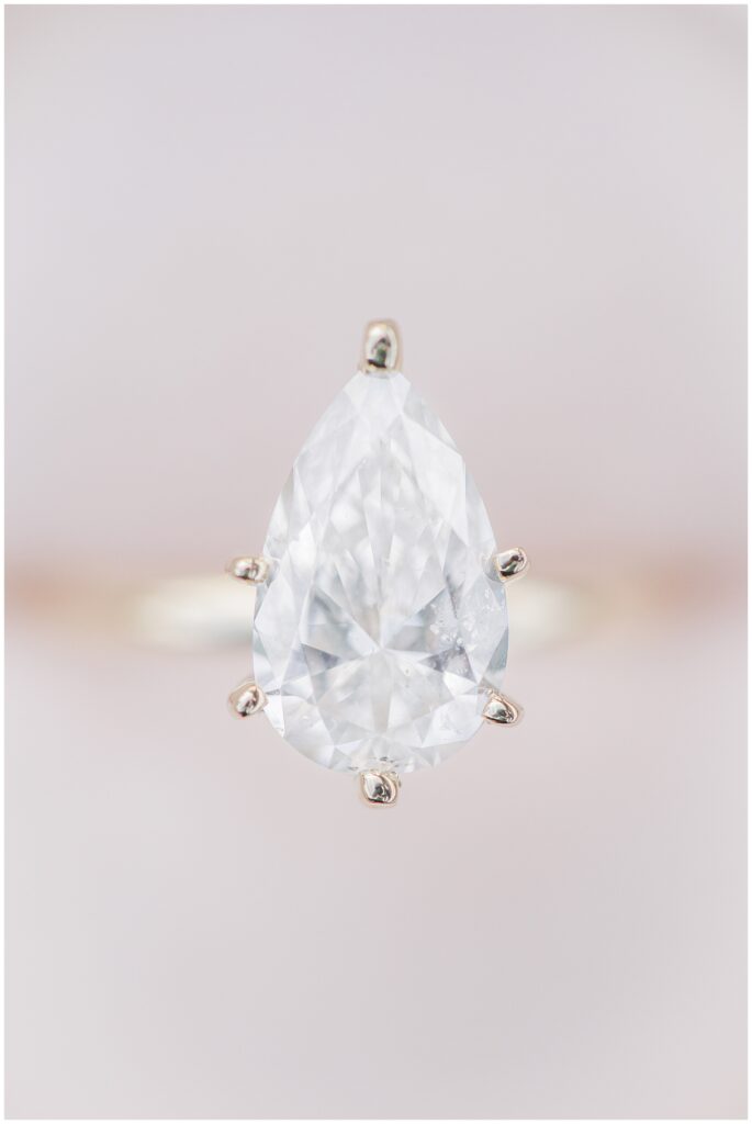 An extreme close-up of a pear-shaped diamond engagement ring showing its facets and six-prong gold setting.