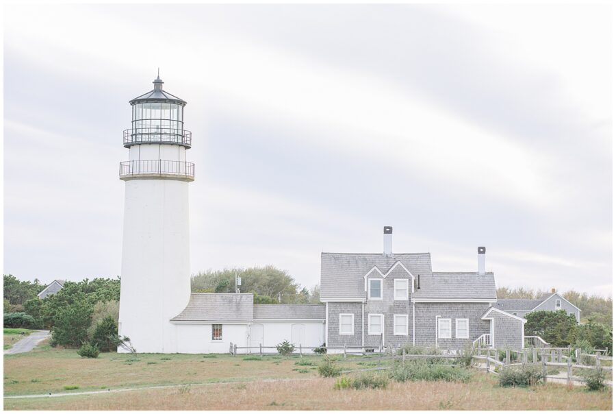A view of Highland Lighthouse and its connected keeper’s house, surrounded by grassy fields under a cloudy sky.