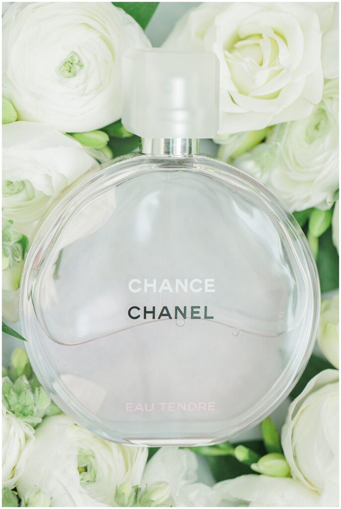 Bottle of Chanel Chance Eau Tendre perfume placed among white ranunculus and rose flowers, photographed as part of wedding detail shots at Nauset Beach Inn.