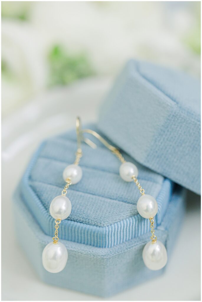 Close-up of gold drop earrings with three pearls each, displayed on a light blue velvet jewelry box.
