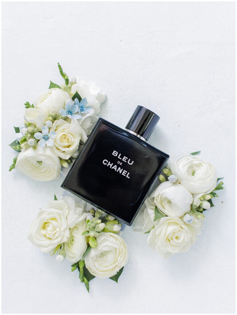 Bottle of Bleu de Chanel cologne surrounded by white roses and small blue flowers, part of the groom’s wedding details at Nauset Beach Inn in Cape Cod.