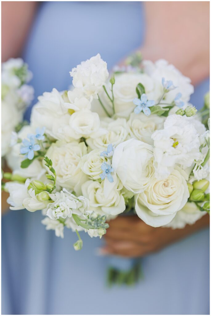 Detail shot of a bridesmaid’s bouquet featuring white roses, ranunculus, and small blue flowers tied with light blue ribbon, photographed during a Nauset Beach Inn wedding in Orleans, MA.