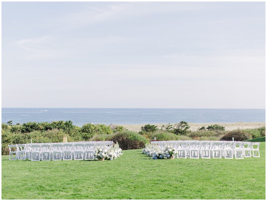 Outdoor wedding ceremony setup on the oceanfront lawn at Nauset Beach Inn in Cape Cod, with rows of white chairs and floral arrangements overlooking the Atlantic Ocean.