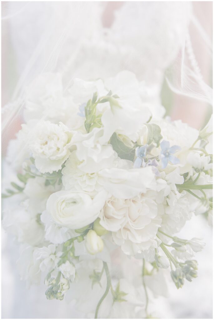 Close-up of the bride’s white bouquet with roses and small blue flowers, softly covered by her veil during a wedding at Nauset Beach Inn in Orleans, MA.