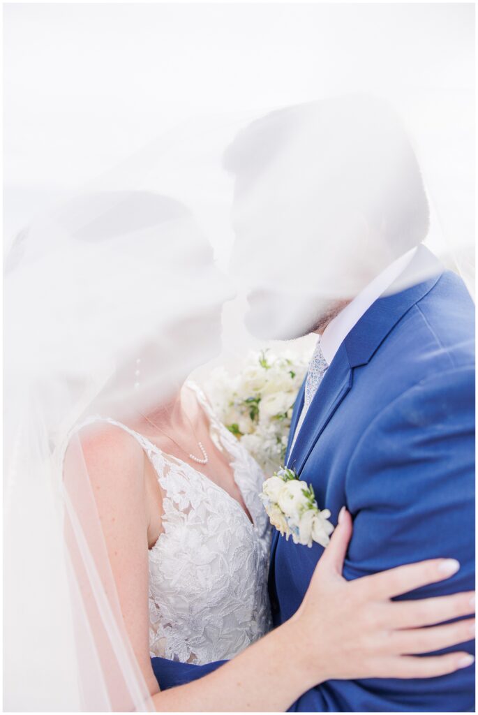 Softly focused image of the bride and groom standing on the sand, their white floral bouquet visible through the veil, during their wedding at Nauset Beach Inn in Orleans, MA.