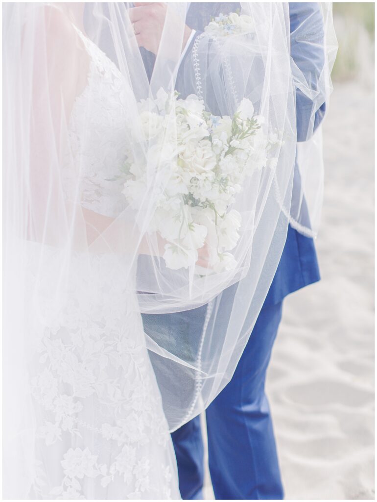 Bride and groom holding florals with a veil over them and the flowers.