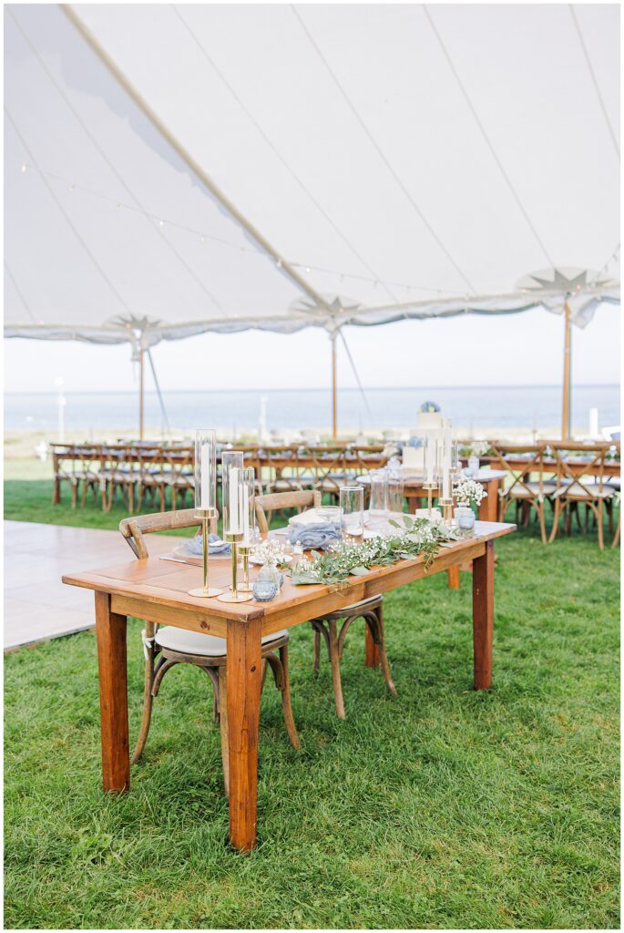 Sweetheart table decorated with white flowers, candles, and greenery under a sailcloth tent overlooking the ocean at Nauset Beach Inn in Cape Cod.