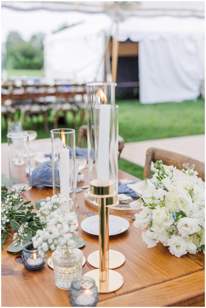 Reception table decorated with white flowers, gold candle holders, and blue accents under a sailcloth tent at Nauset Beach Inn in Orleans, MA.