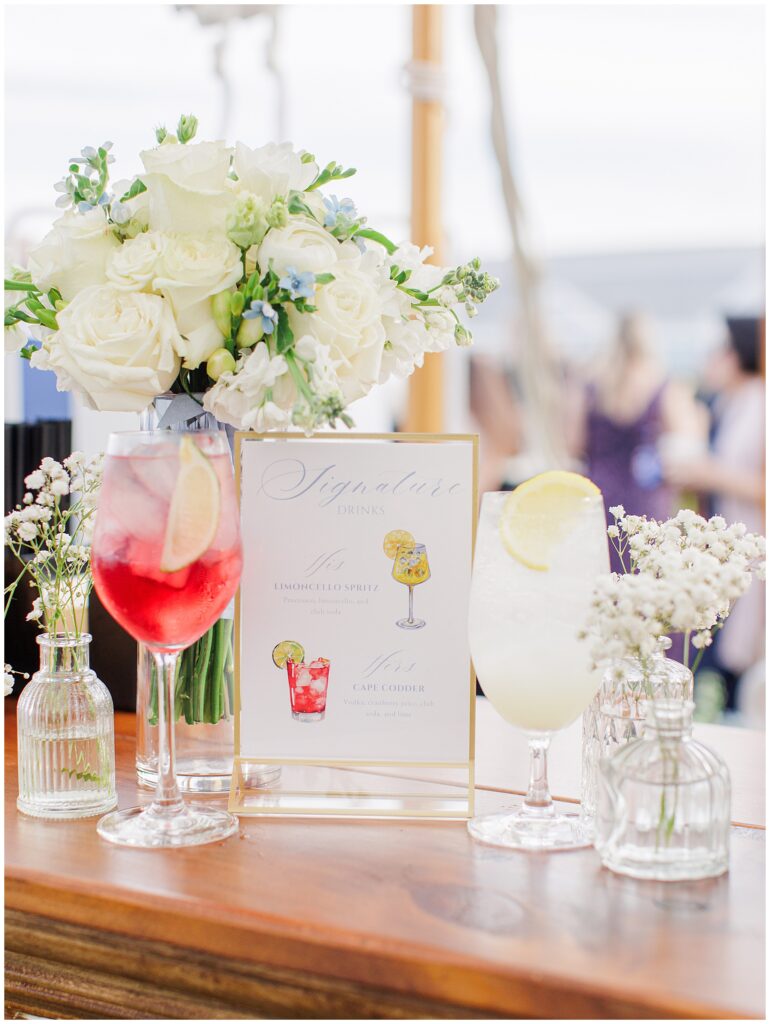 Signature drinks display featuring a Limoncello Spritz and Cape Codder cocktail beside a white floral arrangement at the wedding bar at Nauset Beach Inn in Orleans, MA.
