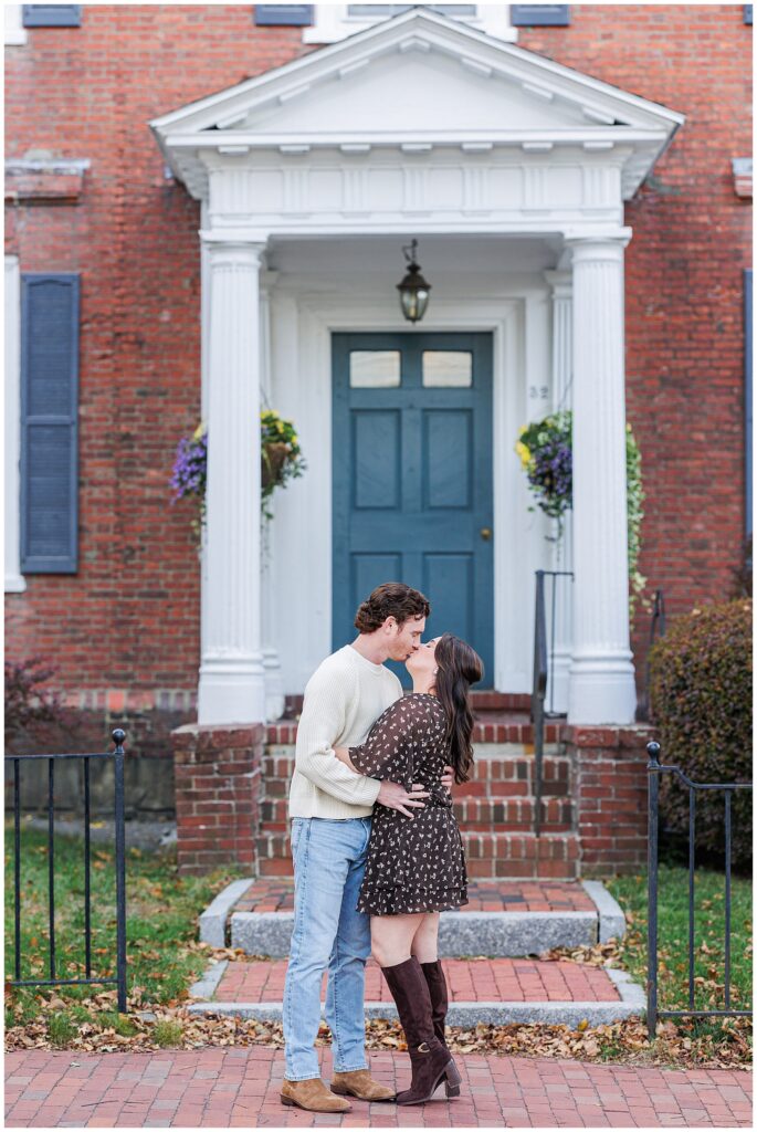 The couple shares a kiss on the brick sidewalk in front of a colonial-style house in downtown Newburyport during their fall engagement shoot.