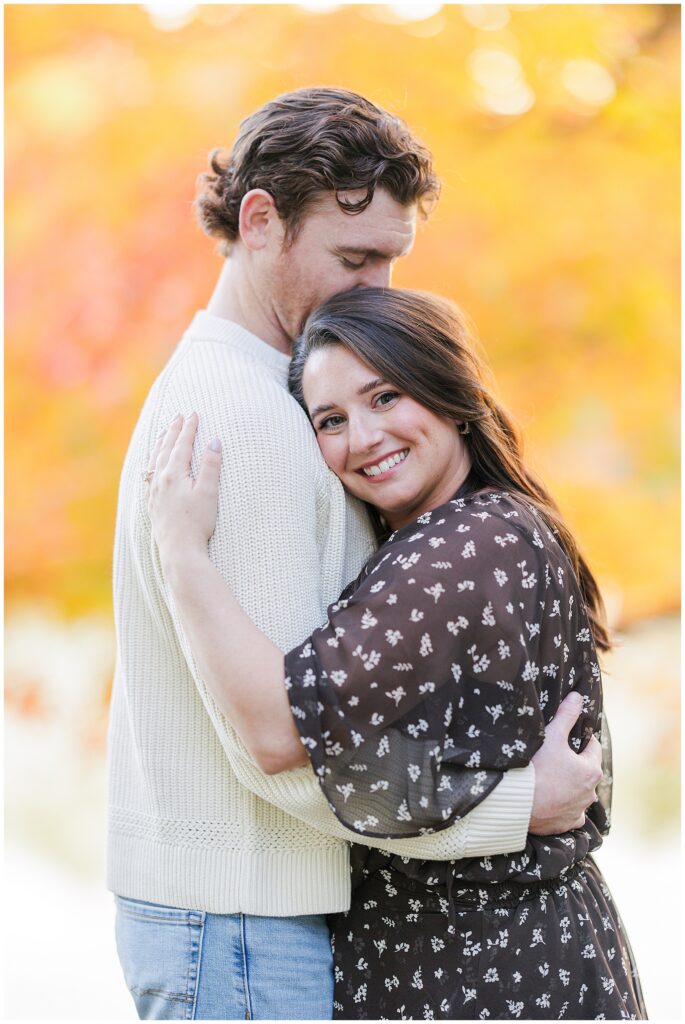 The woman smiles at the camera while hugging her partner beneath glowing fall foliage at Bartlet Mall in Newburyport.