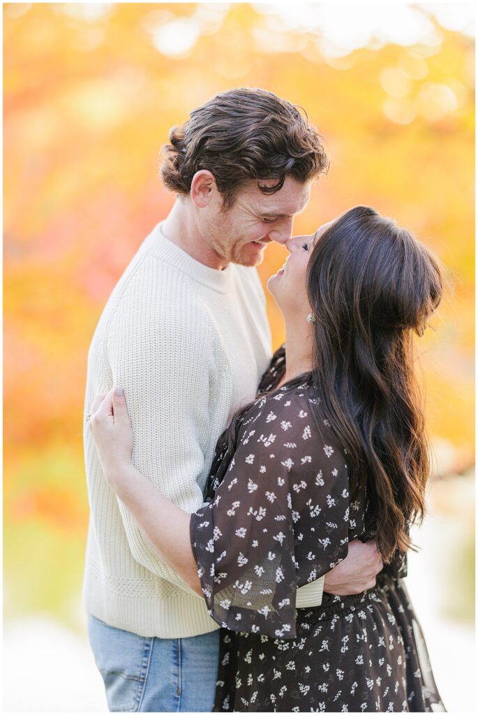 The couple stands forehead to forehead, smiling closely at each other, with vivid autumn leaves in the background at Bartlet Mall in Newburyport, Massachusetts.