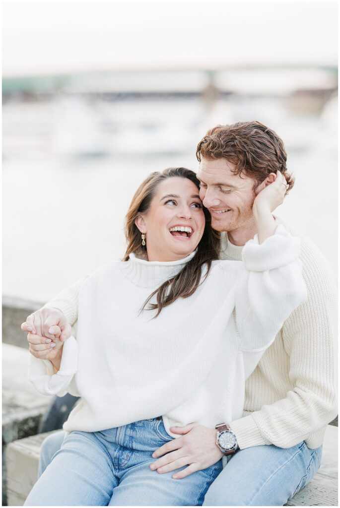 Close-up of the couple sitting on the Newburyport waterfront boardwalk, smiling and holding hands during their engagement session.