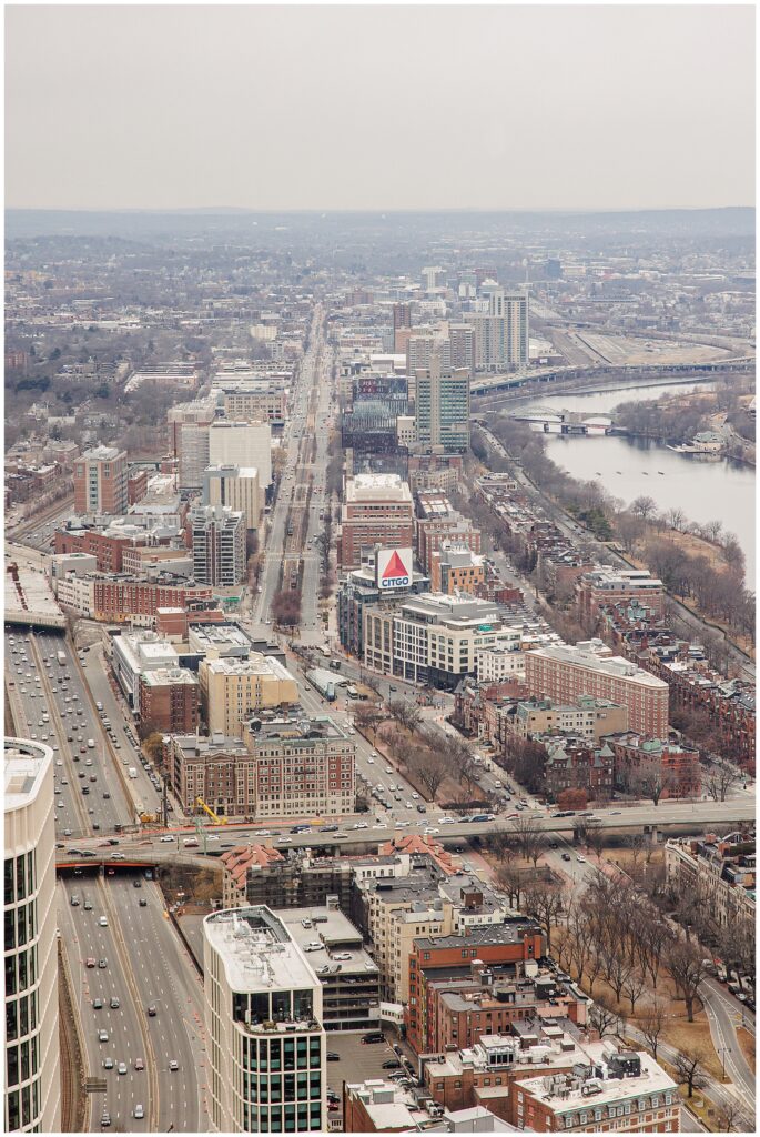 A daytime aerial view facing west from the Prudential Center, showing Kenmore Square, the iconic CITGO sign, Commonwealth Avenue, and the Charles River.