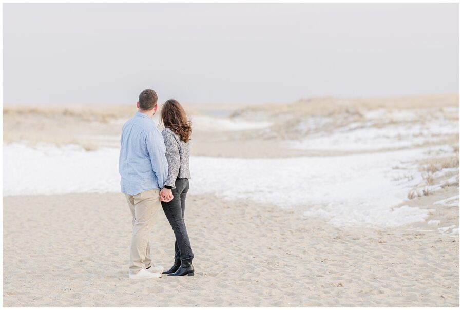 Newly engaged couple standing hand in hand in the sand following their Chatham Lighthouse Beach proposal at Chatham Lighthouse Beach in Chatham, MA Cape Cod.