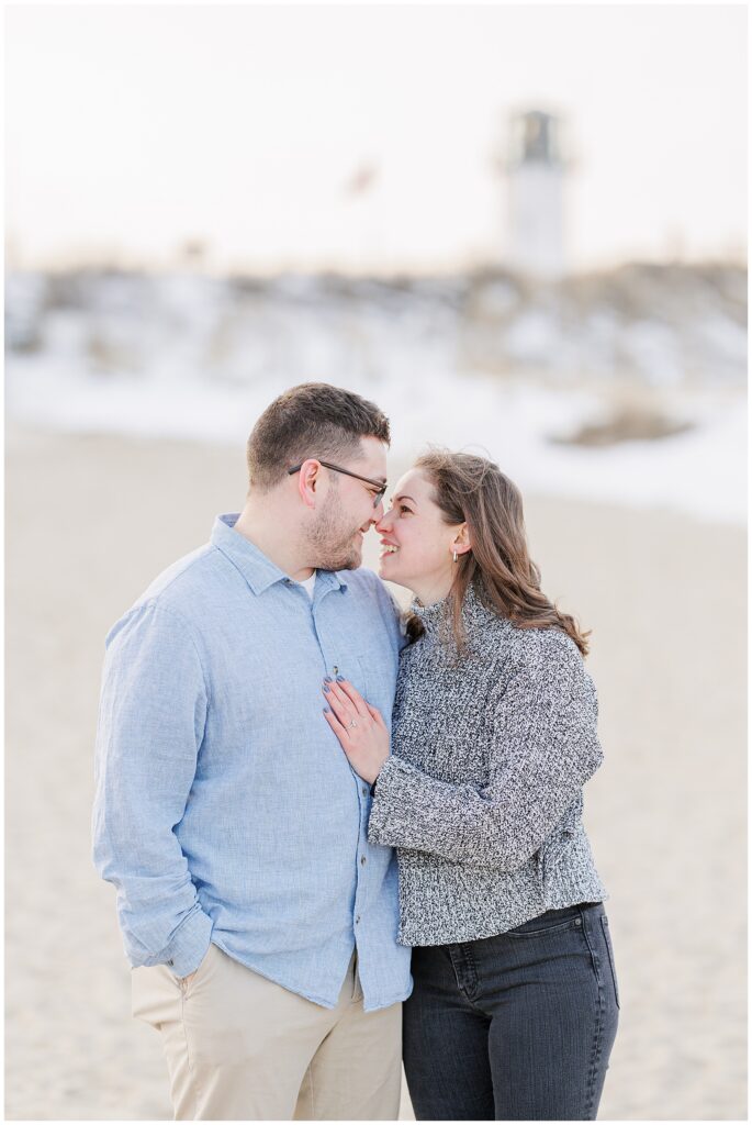Romantic close-up portrait of couple smiling with Chatham Lighthouse in the background after their Chatham Lighthouse Beach proposal in Chatham, MA Cape Cod, captured by a Cape Cod engagement photographer.