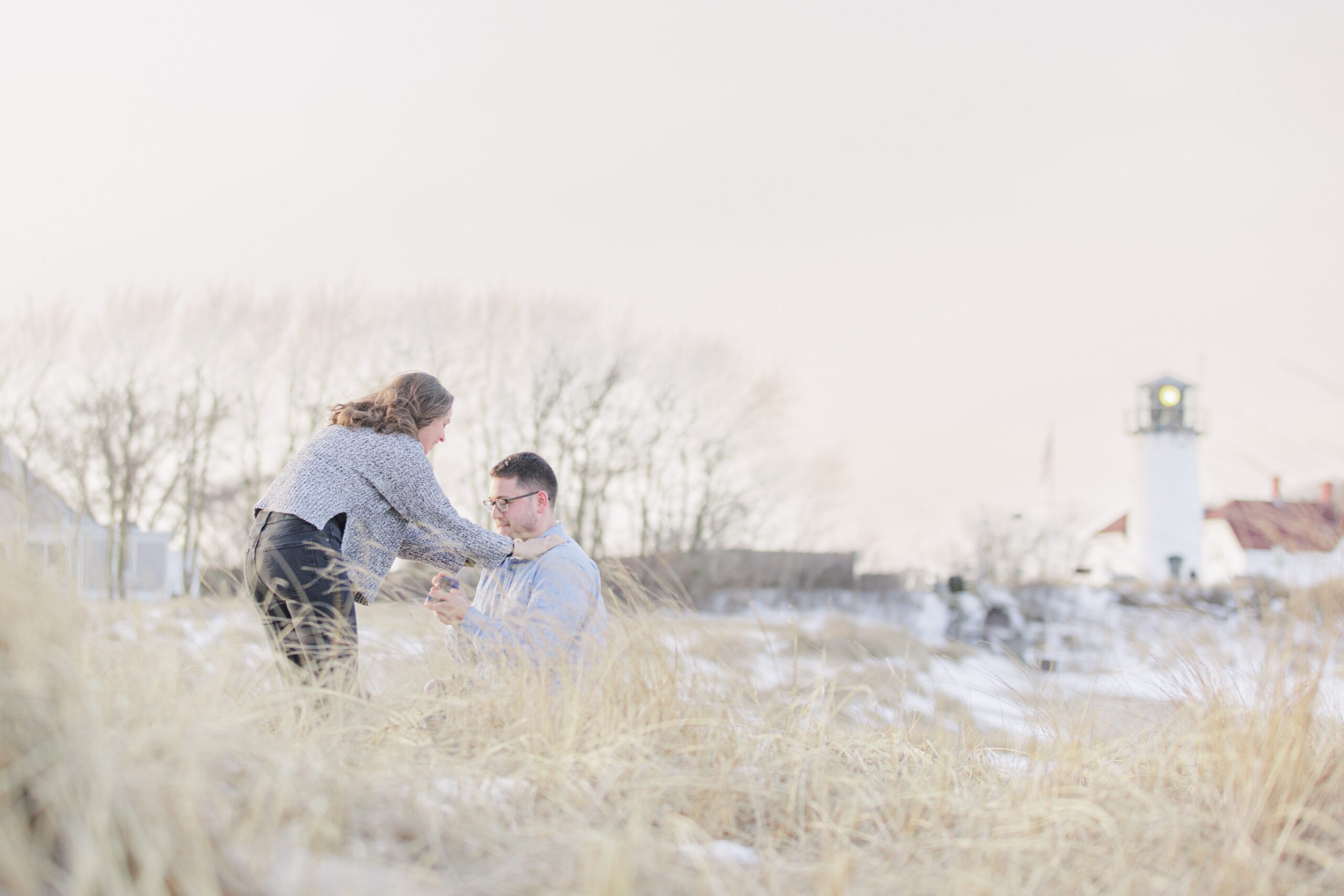 Man proposing on one knee in snowy dunes during a Chatham Lighthouse Beach proposal at Chatham Lighthouse Beach in Chatham, MA Cape Cod.