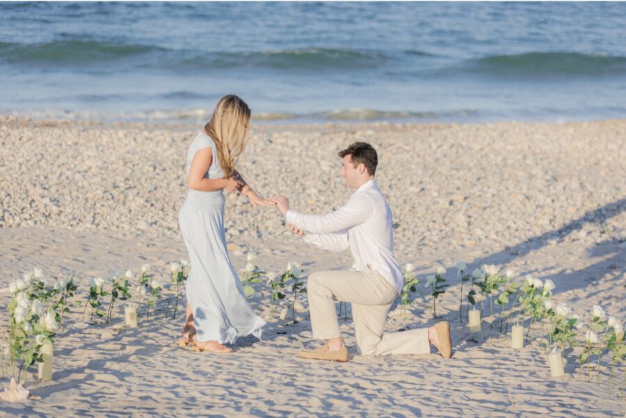 Close up of man placing engagement ring on woman’s finger during a beach proposal