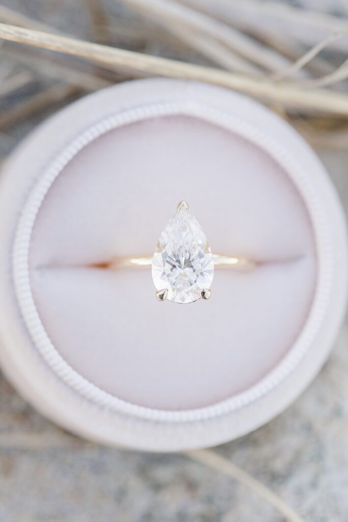 Close up of pear shaped diamond engagement ring in velvet box on the beach