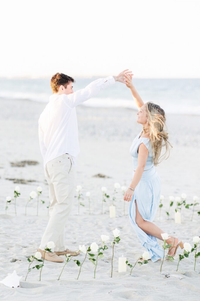 Couple twirling and celebrating inside a circle of white roses after Duxbury Beach proposal