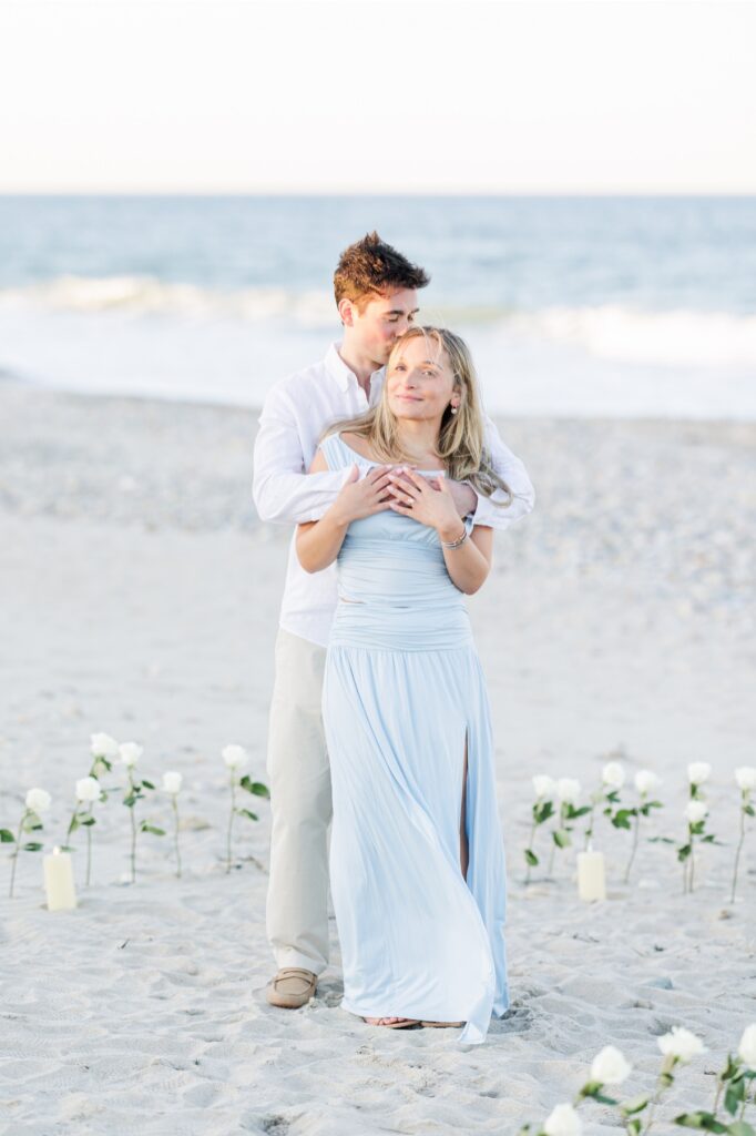 Romantic portrait of couple embracing on Duxbury Beach surrounded by white roses