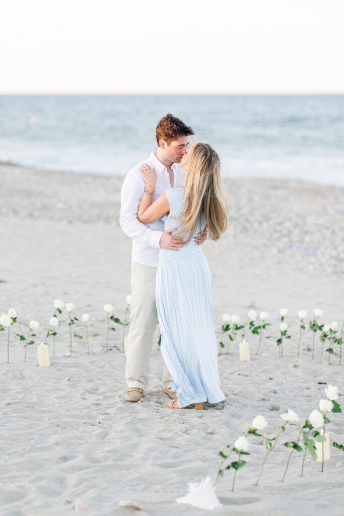 Couple kissing on the beach after a romantic Duxbury Beach proposal with ocean in background
