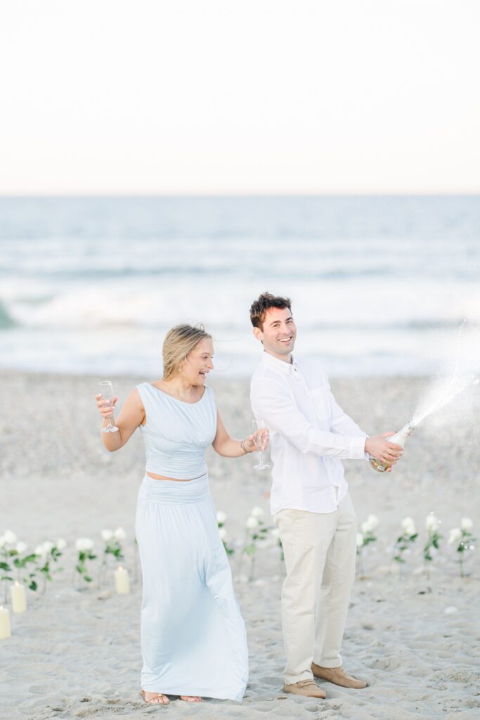 Just engaged couple popping champagne and celebrating on Duxbury Beach