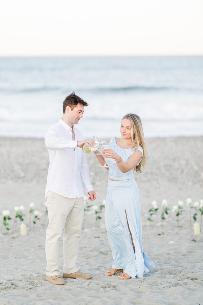Couple pouring champagne into glasses on the beach after their proposal