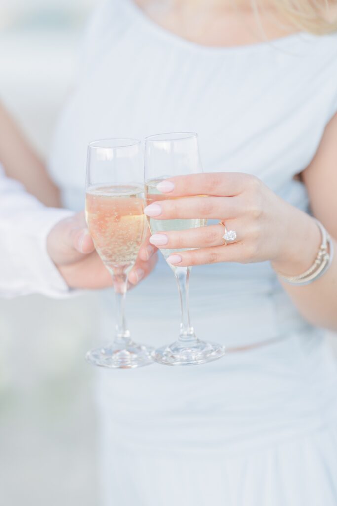 Close up of champagne toast with engagement ring visible during beach proposal celebration