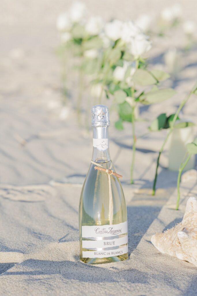 Champagne bottle on the sand with white roses during Duxbury Beach proposal celebration