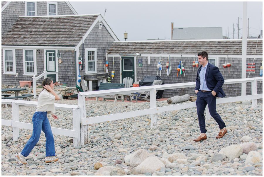Couple walking toward each other on rocky beach before Scituate Lighthouse proposal in Scituate Massachusetts