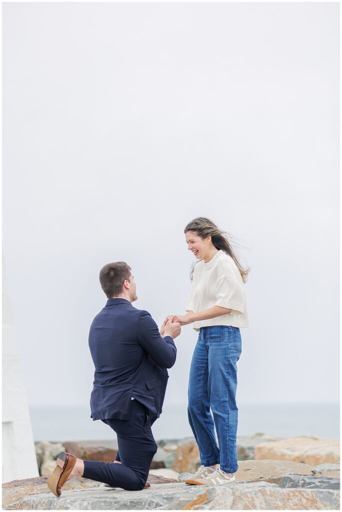Close up of emotional Scituate Lighthouse proposal with man on one knee holding partner’s hands