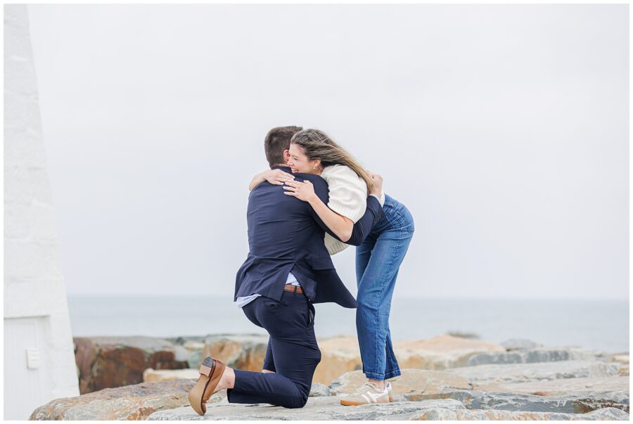 Joyful reaction during Scituate Lighthouse proposal as couple embraces on rocky shoreline in Scituate MA