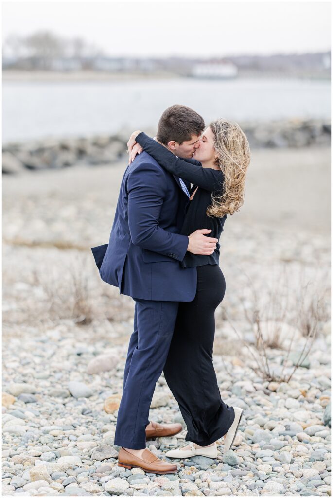 Couple kissing on rocky beach after Scituate Lighthouse proposal with ocean in background