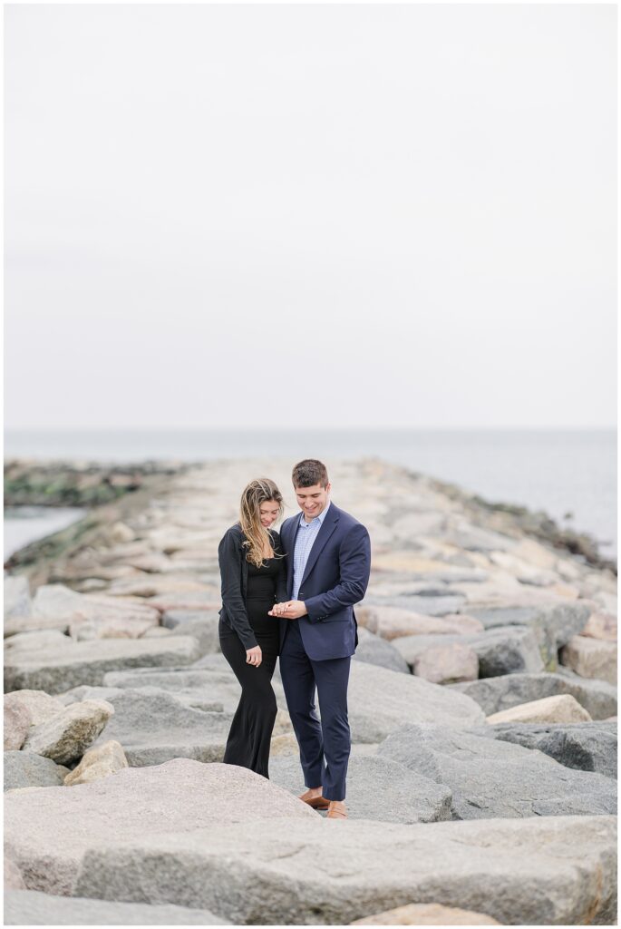 Bride to be admiring engagement ring while walking on rocks after Scituate Lighthouse proposal
