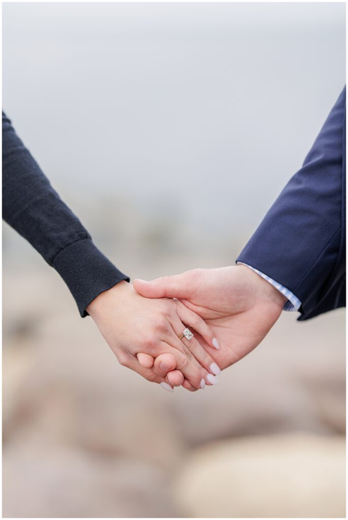 Close up of couple holding hands with engagement ring during Scituate Lighthouse proposal