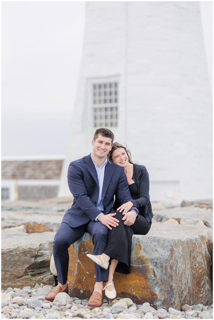 Couple sitting on coastal rocks in front of lighthouse after Scituate Lighthouse proposal in Scituate MA