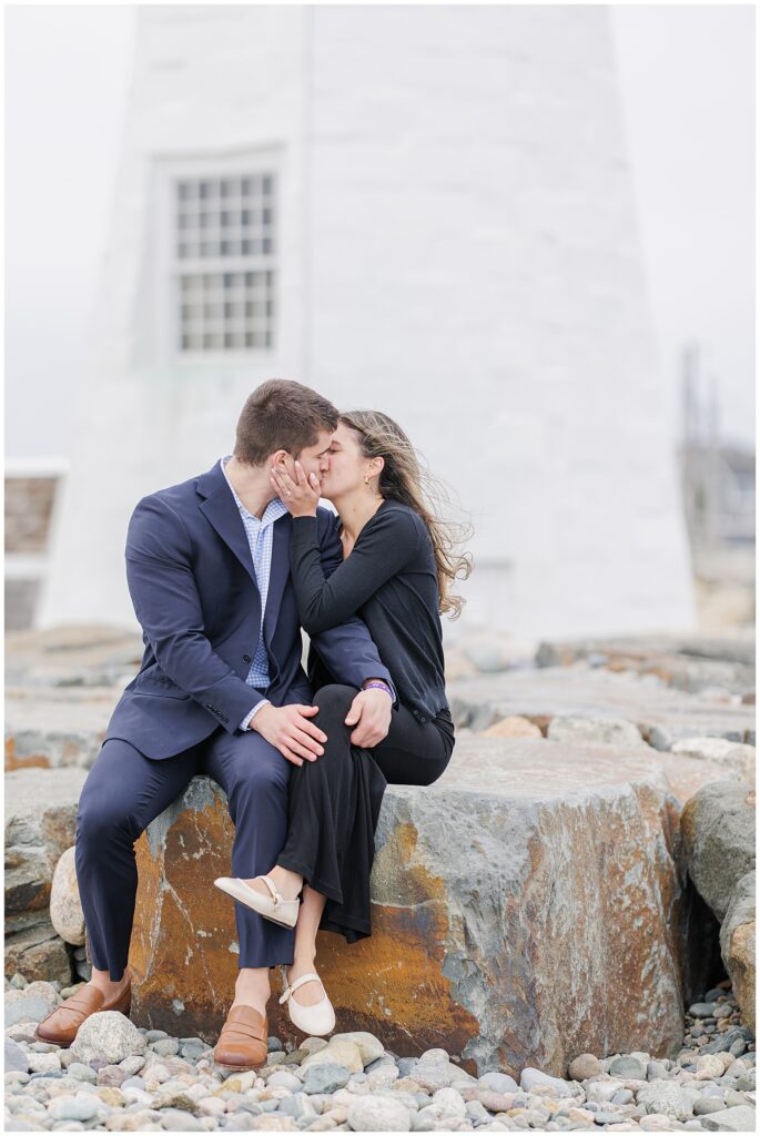 Couple kissing while seated on rocks after Scituate Lighthouse proposal session