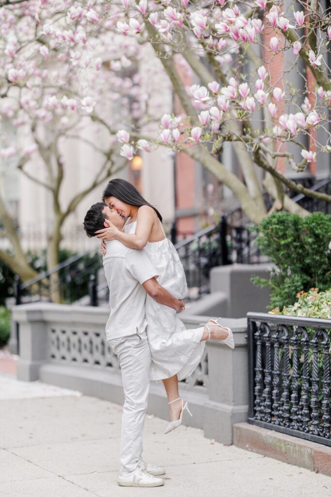     Couple embracing beneath blooming magnolia trees on Beacon Hill during romantic Beacon Hill engagement photos in Boston