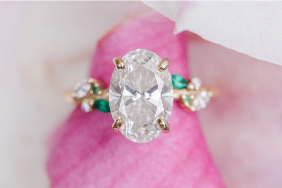     Oval diamond engagement ring with emerald accents photographed on a pink magnolia flower during Beacon Hill engagement photos