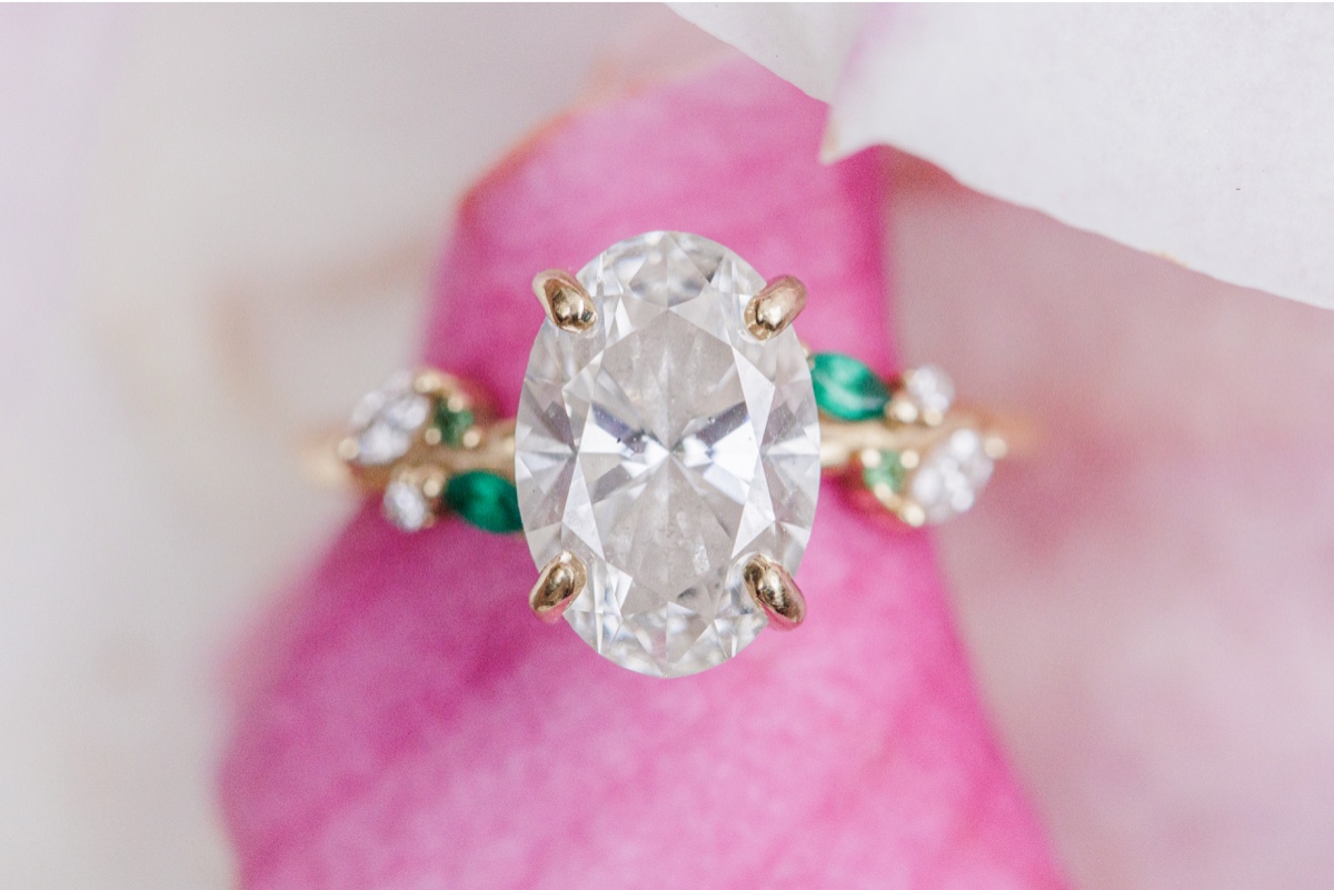Oval diamond engagement ring with emerald accents photographed on a pink magnolia flower during Beacon Hill engagement photos