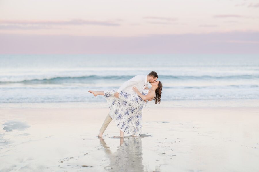     Joyful Seabrook Beach engagement photo of a couple sharing a kiss during a playful dip pose at sunset.
