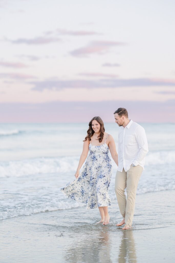     Romantic New Hampshire engagement photos of a couple walking barefoot through the ocean waves at sunset.