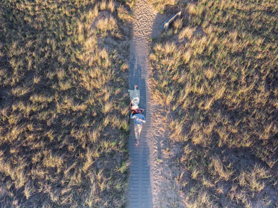     Drone photo of a couple lying together on a sandy beach path surrounded by dune grass in Seabrook, New Hampshire.