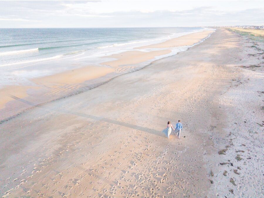    Aerial New Hampshire engagement photos of a couple walking along the shoreline at Seabrook Beach.