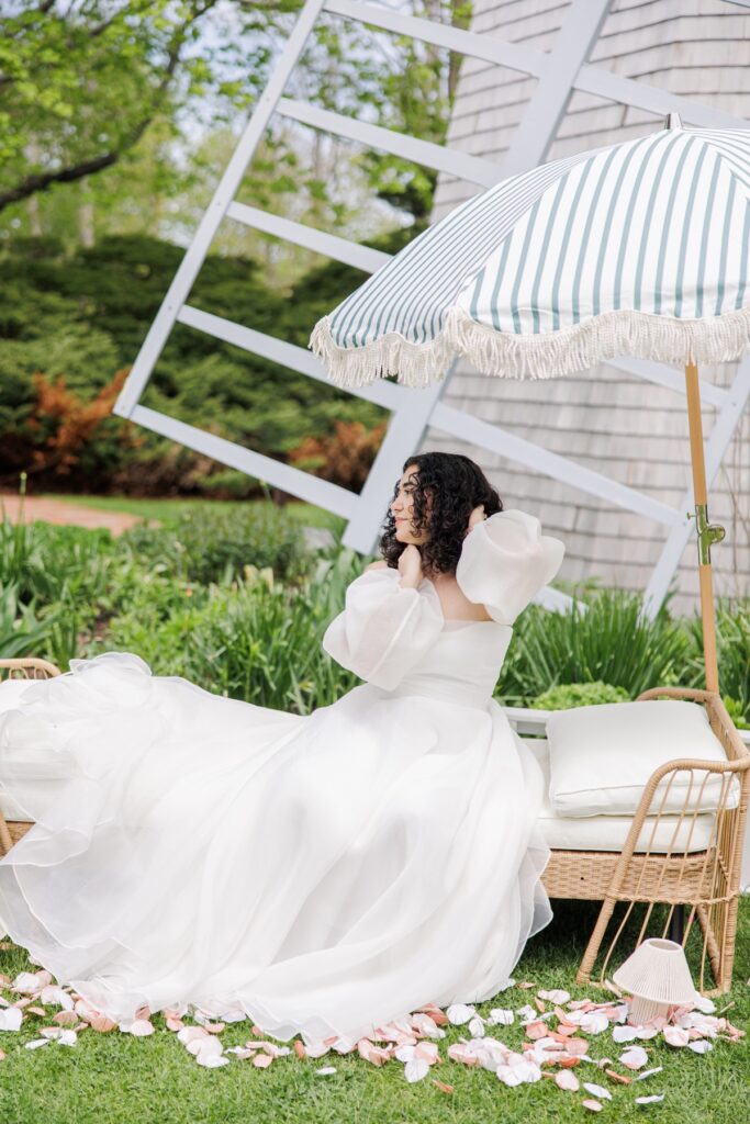 Bride seated beneath a striped umbrella beside the windmill at Heritage Museums & Gardens in Sandwich Massachusetts
